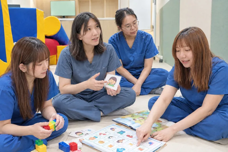 治療師們坐在兒童室的地墊上，拿著圖卡和積木